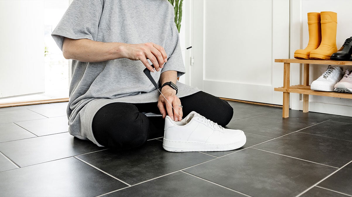 En person sitter på gulvet og måler innermålet på en hvit sneaker med målepinnen