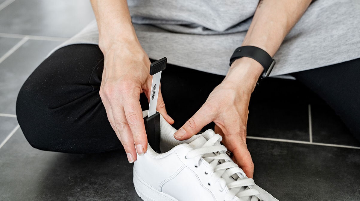 En person sitter på gulvet og måler innermålet på en hvit sneaker med målepinnen